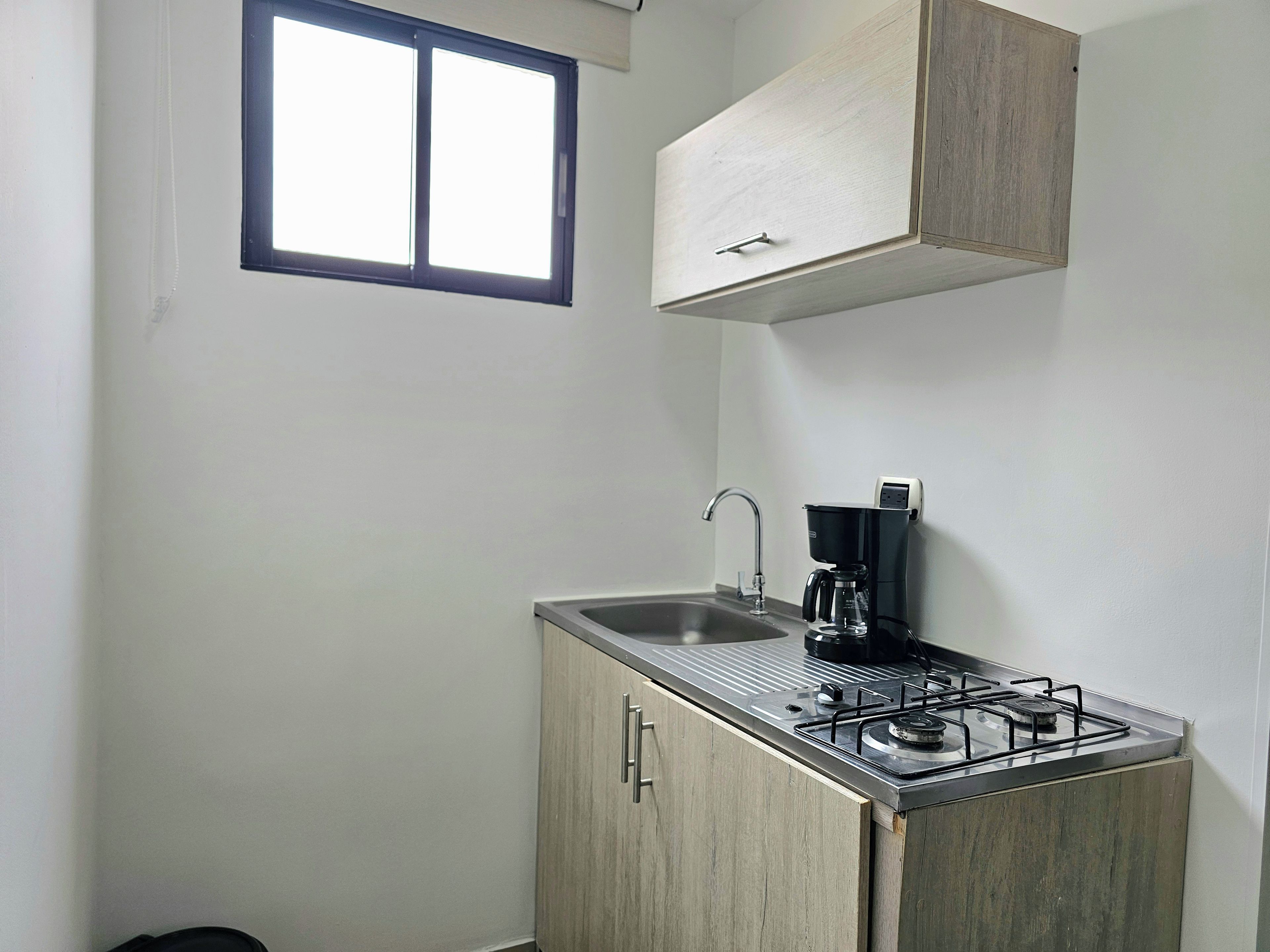 A compact kitchenette with a gas stove, a coffee maker, and a sink.