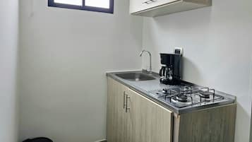A compact kitchenette with a gas stove, a coffee maker, and a sink.