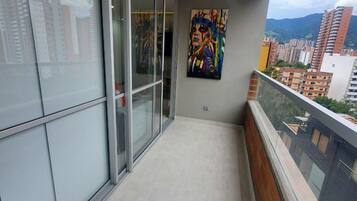 Un balcón con puerta corrediza de vidrio que da a un espacio interior, un cuadro en la pared y vistas de edificios circundantes.
