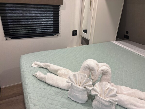 A bed with a quilted green cover and a pair of white towels folded on it.