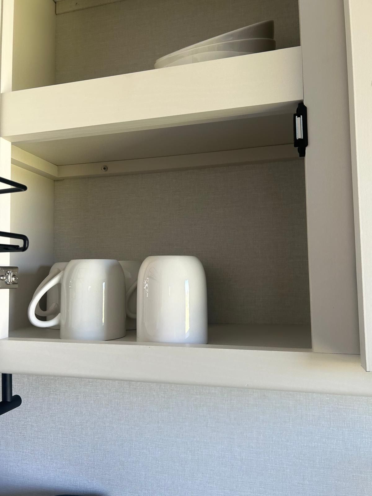 A white cabinet with two white mugs on the lower shelf.