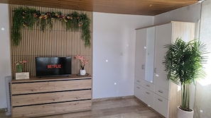 A modern living room with a wooden entertainment unit, a flat-screen TV displaying the Netflix logo, a potted plant, and a large wardrobe. - Vacation Rental Near Rothenburg / Romantic Franconia (Colmberg)