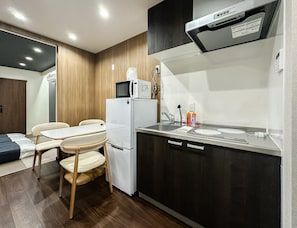 A compact kitchenette with a microwave, refrigerator, and sink. There is a small dining area with a table and chairs. - HANASTAY NIWA (Osaka)