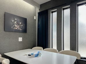 A conference room with a white table, beige chairs, a painting on the wall, and a window with curtains. - HANASTAY NIWA (Osaka)