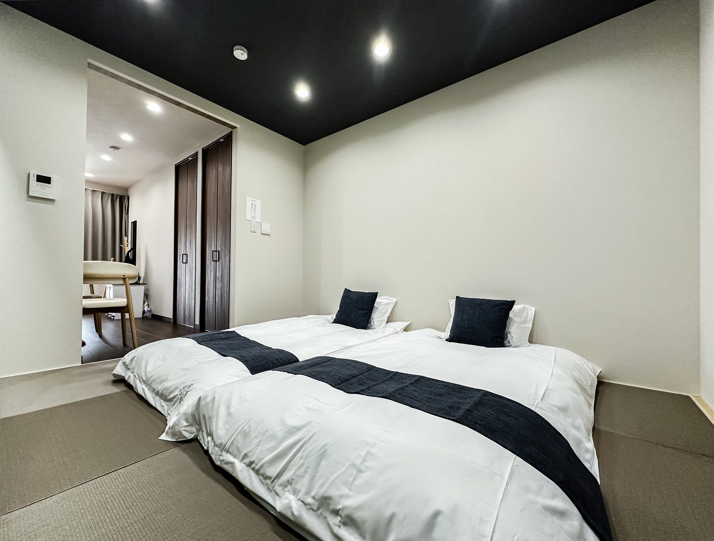 Habitación de hotel con dos camas, un escritorio y un baño visible a través de una puerta abierta.