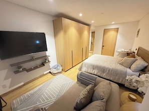 Quarto moderno com televisão, duas camas, guarda-roupa e mesa de cabeceira.