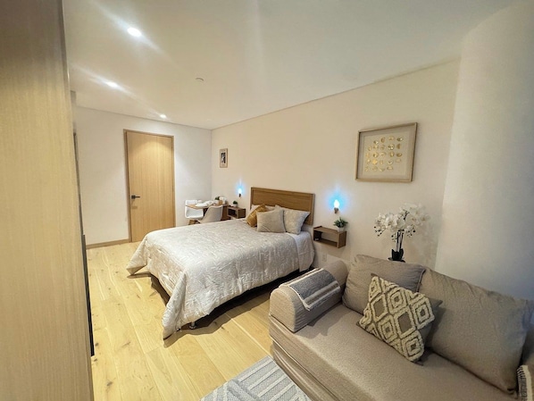 Un dormitorio con cama, sofá, escritorio y una silla.