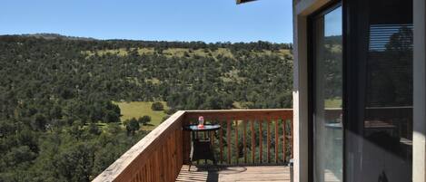Una terraza de madera con una mesa y sillas, con vistas a un paisaje montañoso y frondoso.