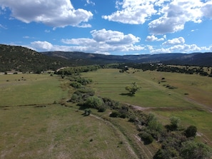 A panoramic view of a rural landscape with rolling hills, scattered trees, and a clear sky.