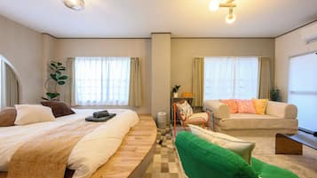 A hotel room with a bed, a sofa, a chair, a small table, and a plant.