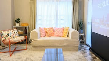 A living room with a sofa, a chair, a coffee table, a screen, and a plant.