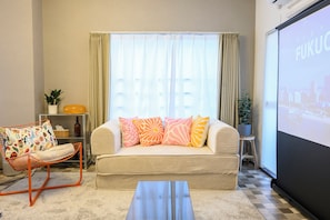 A living room with a sofa, a chair, a coffee table, a screen, and a plant. - Zeroichi Hotel Art Ohori  (Fukuoka)