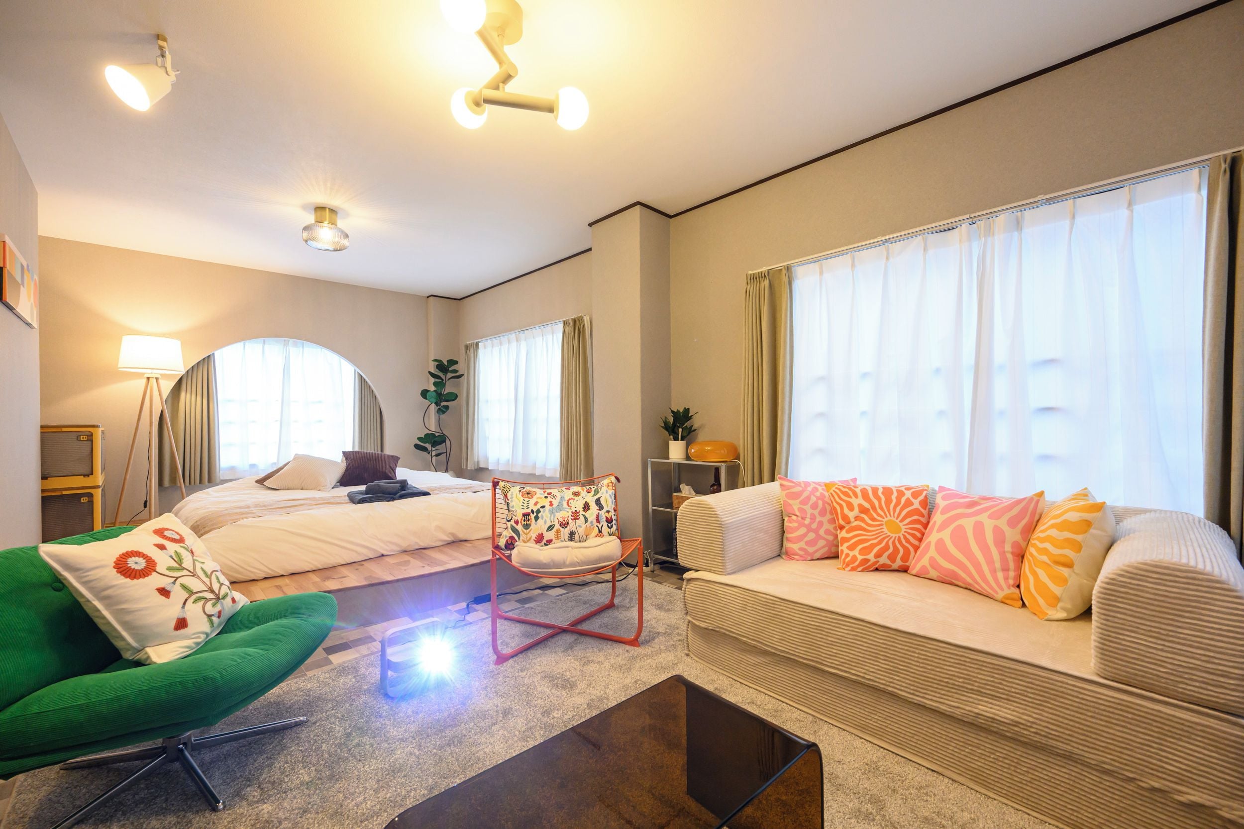 A hotel room with a bed, a sofa, a green armchair, a coffee table, and a floor lamp.