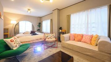 A hotel room with a bed, a sofa, a green armchair, a coffee table, and a floor lamp.