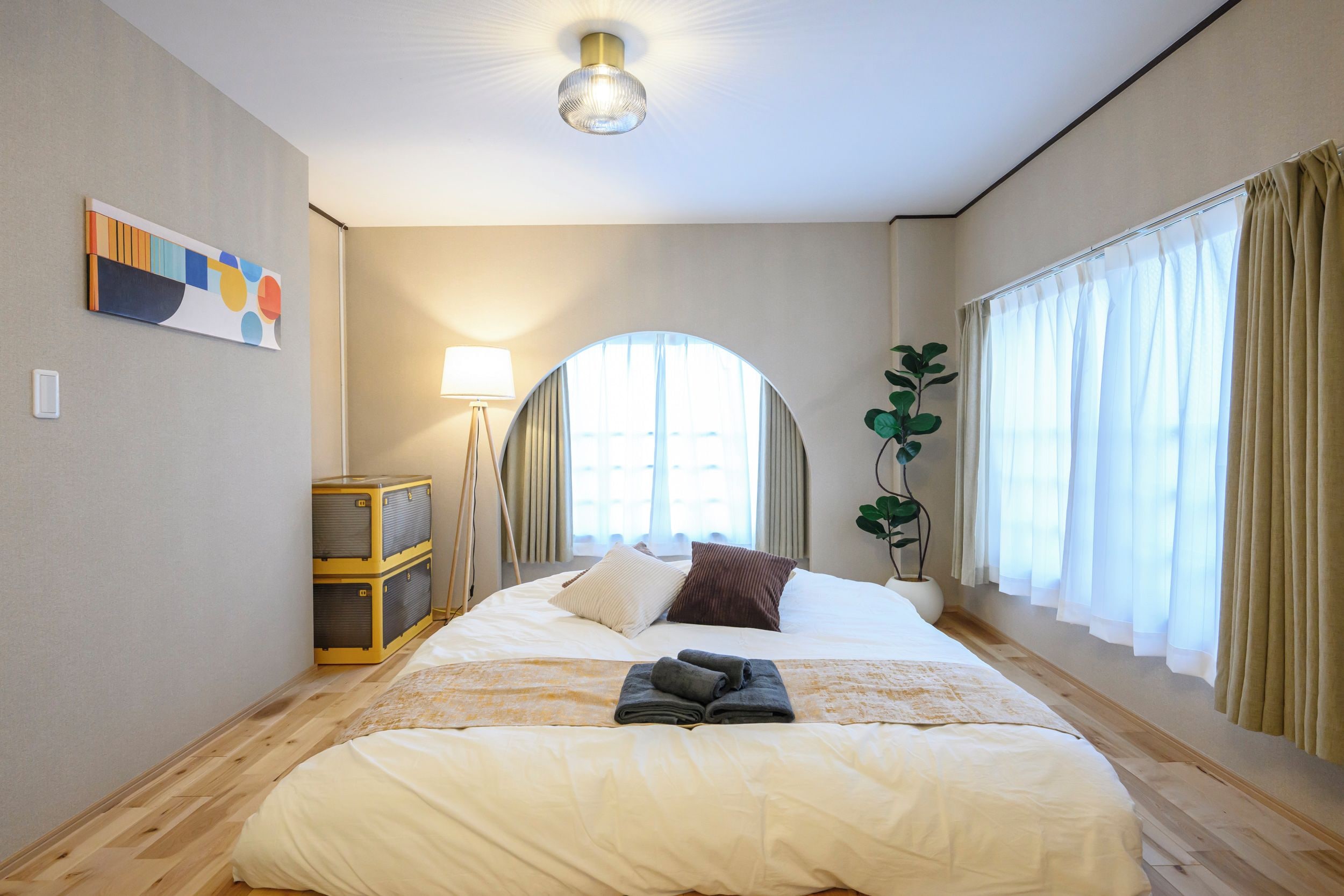 A hotel room with a bed, a lamp, a plant, and a window with curtains.