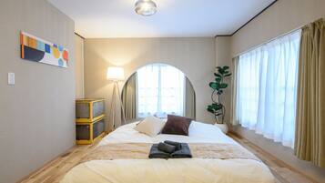 A hotel room with a bed, a lamp, a plant, and a window with curtains.