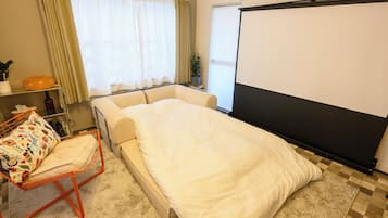 A hotel room with a bed, a small table with a plant, a chair, and a projector screen.