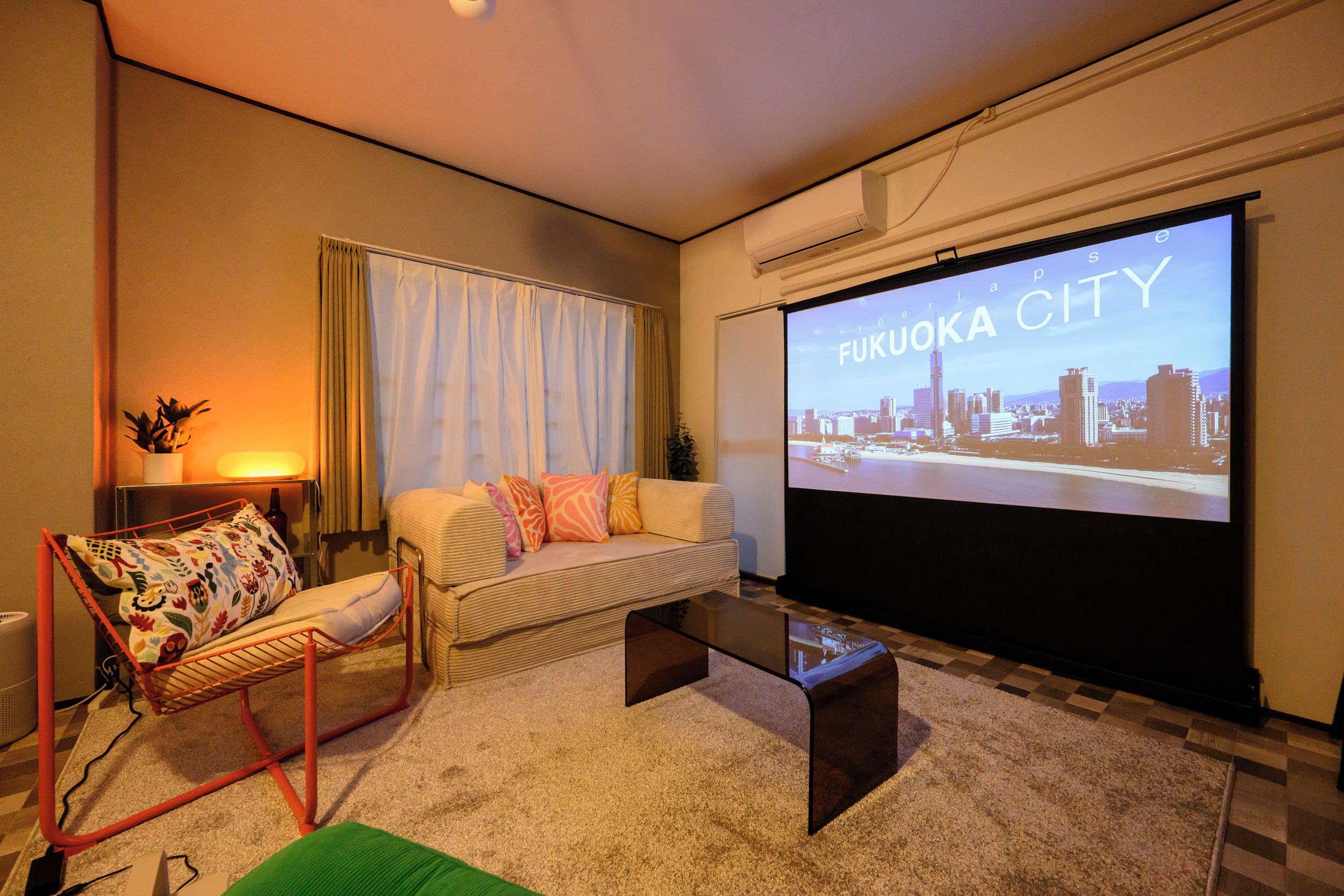 A modern living room with a sofa, a red chair, a coffee table, and a large screen displaying a cityscape.