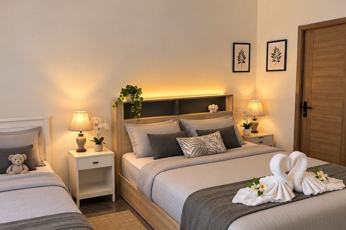 Habitació d'hotel amb dos llits, un panell frontal de fusta, taules de nit amb làmpades, una petita planta en test i un arranjament decoratiu amb tovalloles.
