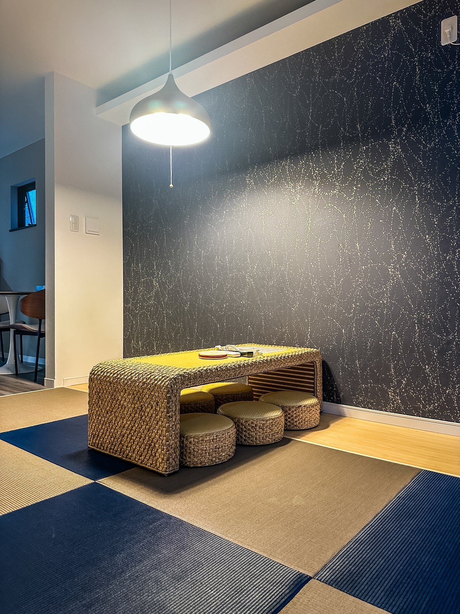 A room with a woven bench, a hanging light fixture, and a dark textured wall.
