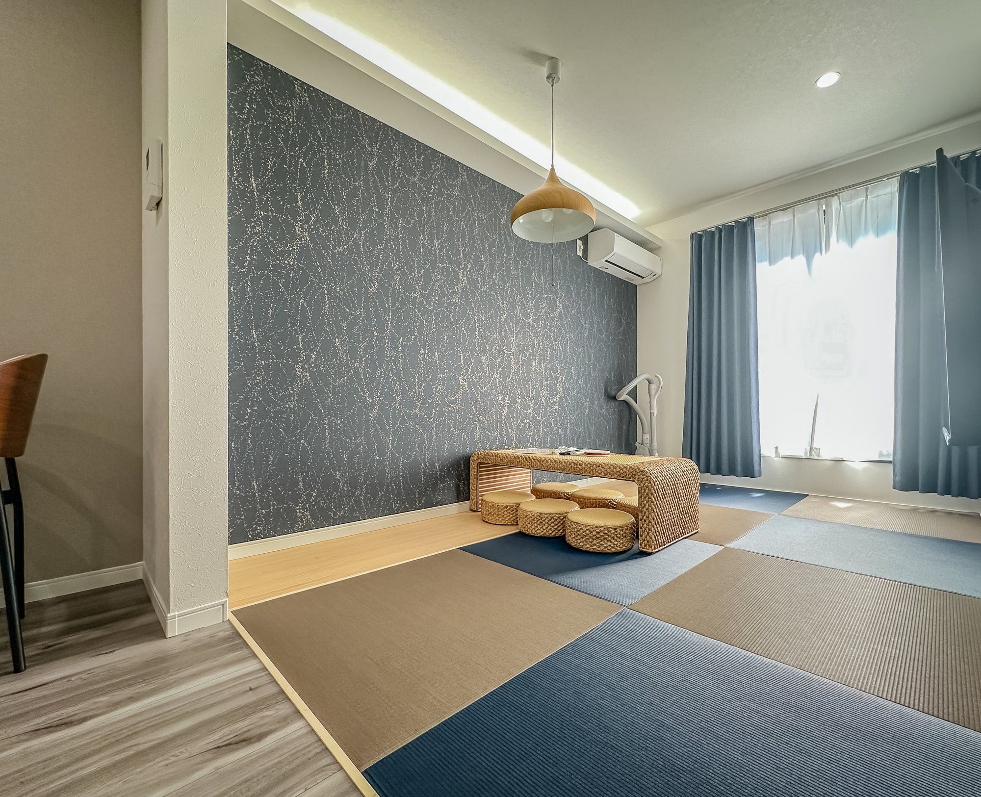 A room with tatami mats, a woven bench, a hanging light fixture, and a large window with curtains.