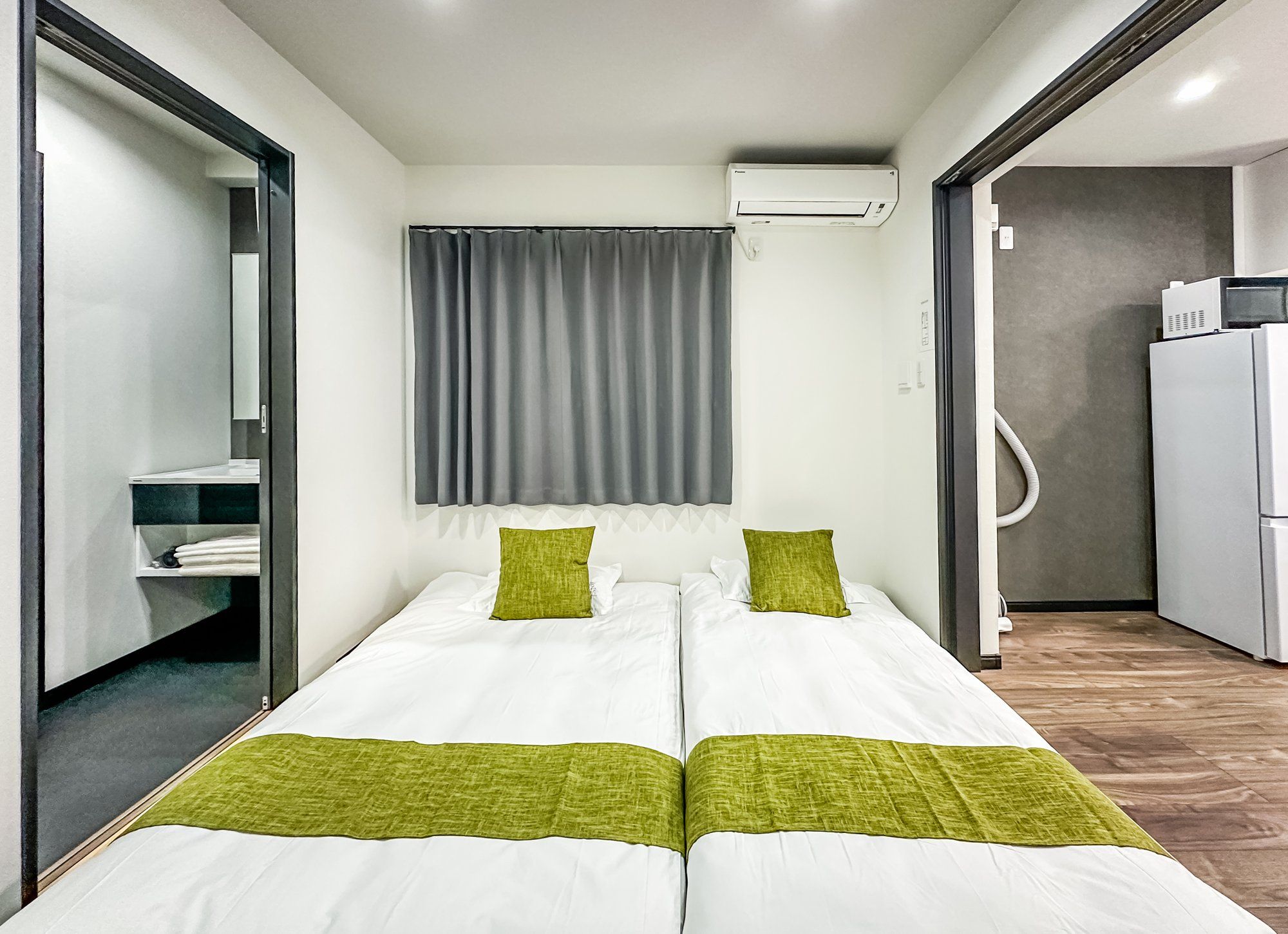 A double bed with two pillows, a grey curtain, and an air conditioning unit above it.