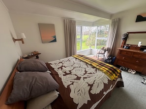 A bedroom with a large bed, a dresser, a chair, and a window with a view of greenery.