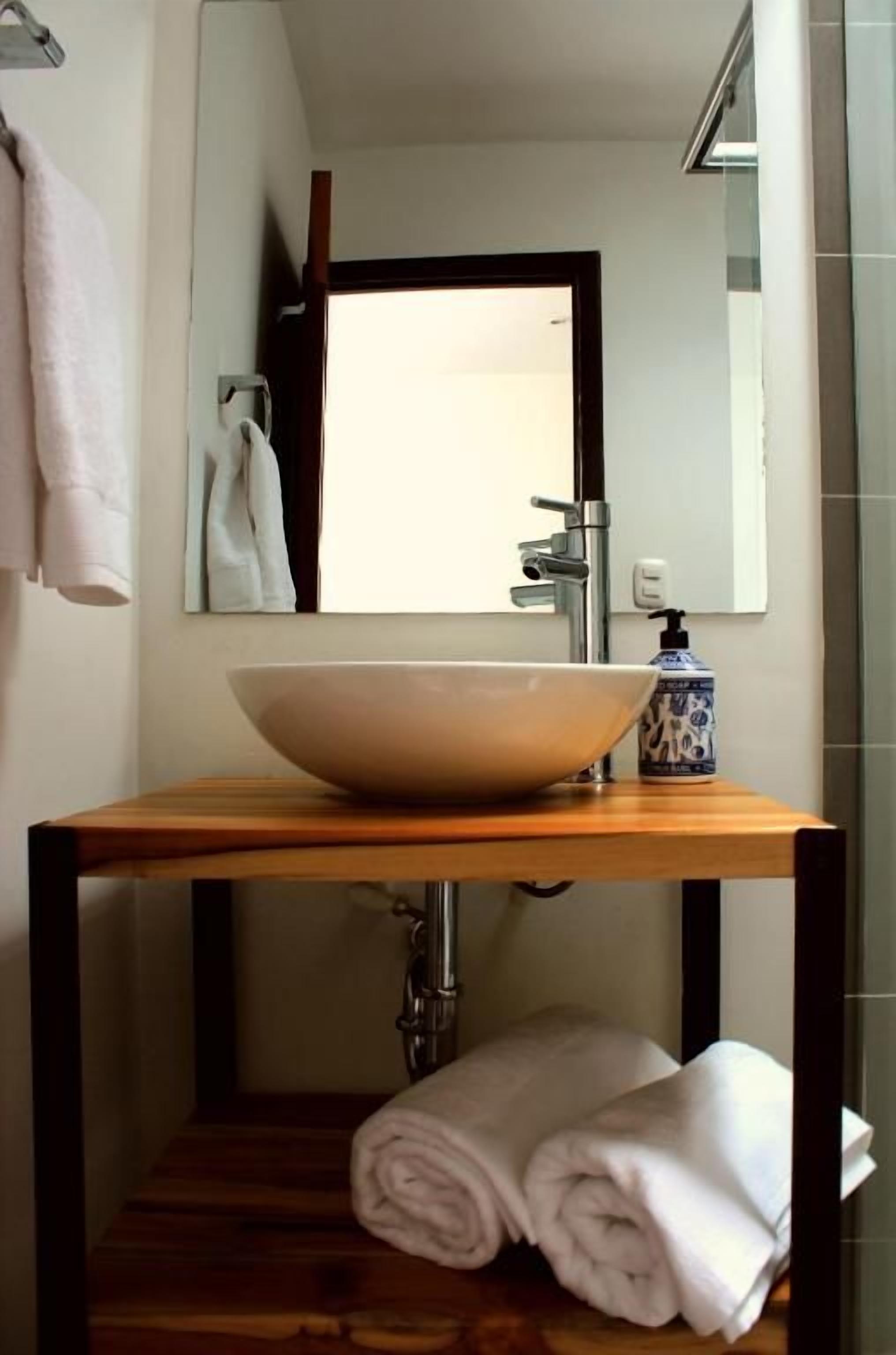 Un baño con un lavamanos grande tipo cuenca, un espejo y un perchero para toallas.