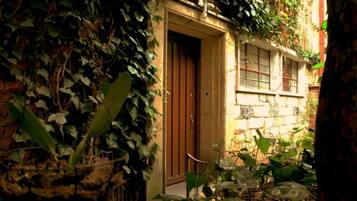 Un callejón estrecho con una puerta que da a un edificio, rodeado de follaje denso.
