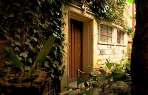 A narrow alleyway with a door leading to a building, surrounded by dense foliage. - Casa Muntu (Bogotá)