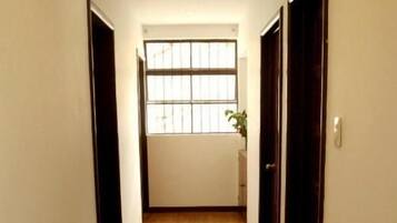 Un pasillo con suelo de madera, un tragaluz y una ventana con barrotes.