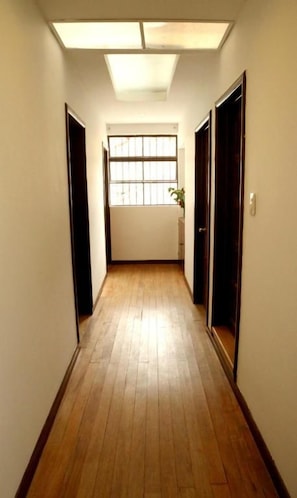 A hallway with wooden flooring, a skylight, and a window with bars. - Casa Muntu (Bogotá)
