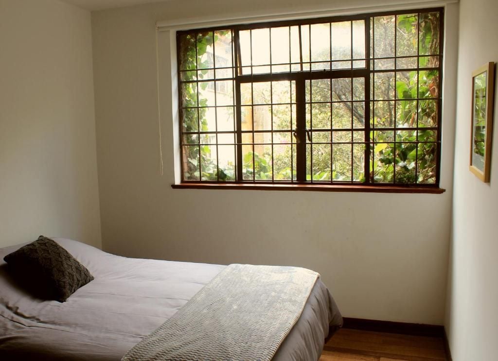 Un dormitorio con una cama, una ventana con rejas y vista a follaje exterior.
