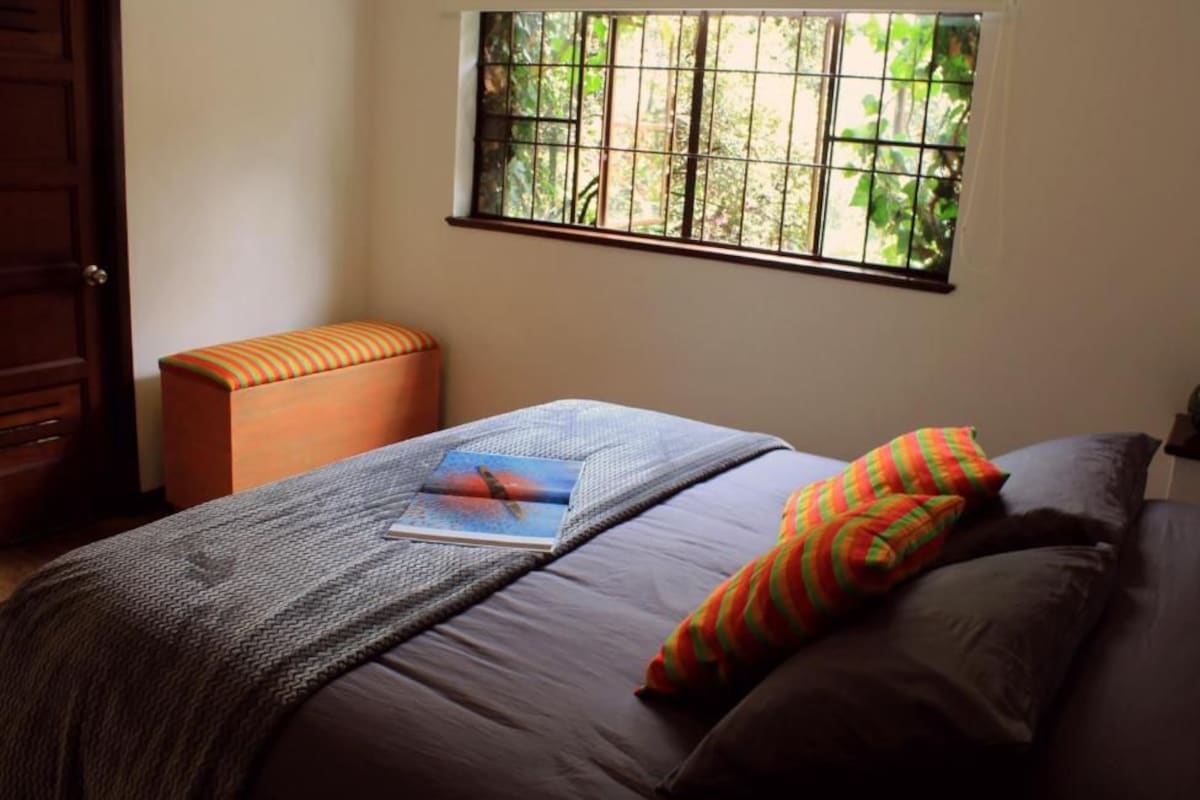A bedroom with a bed, a window with bars, a door, and a small table.