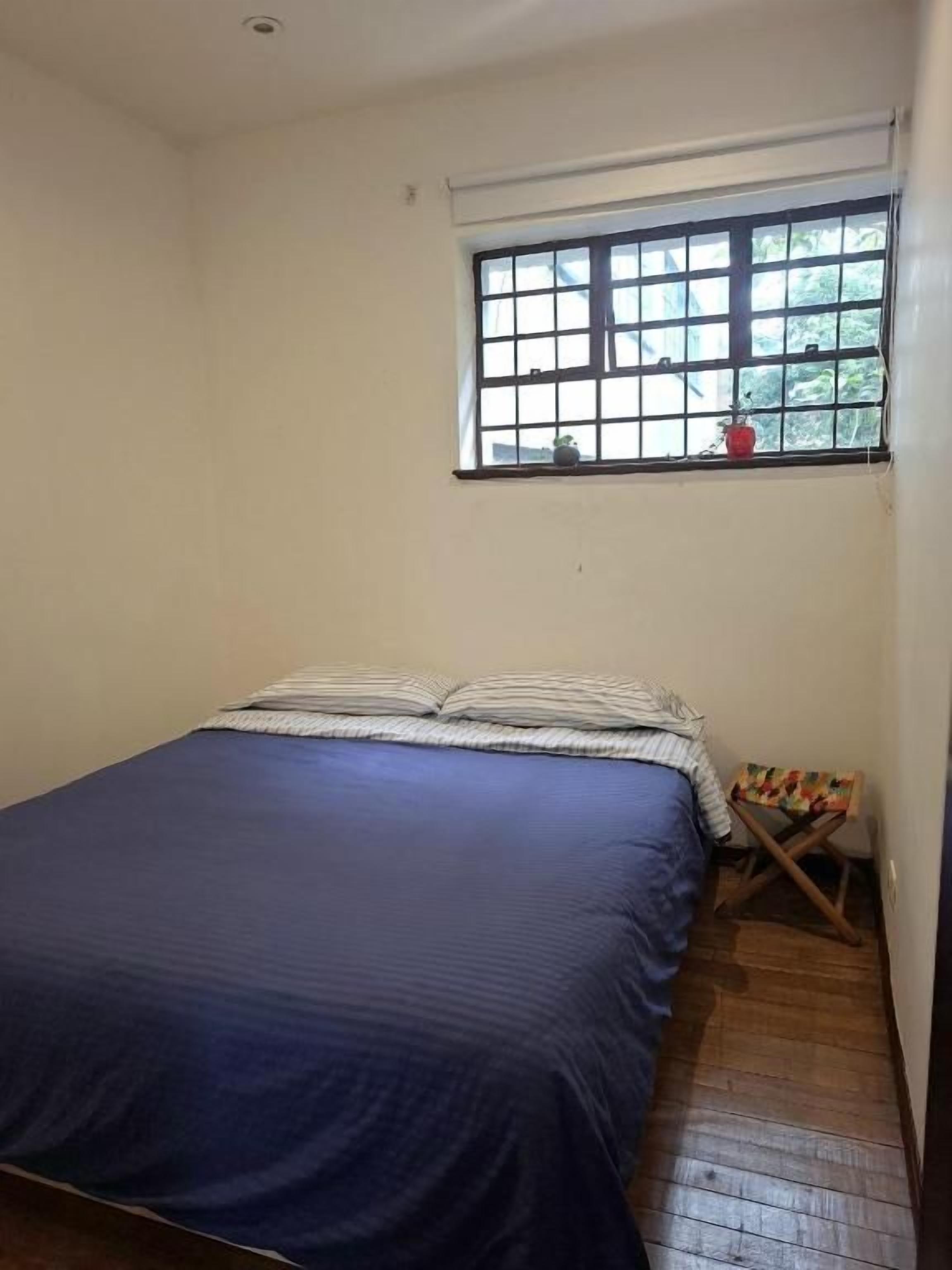 Un dormitorio con una cama, un ventanal y suelo de madera.