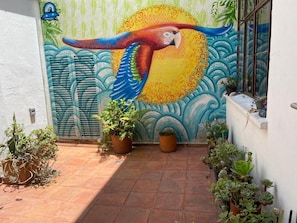 A mural of a parrot on a wall, potted plants, and a tiled patio area. - Casa Muntu (Bogotá)
