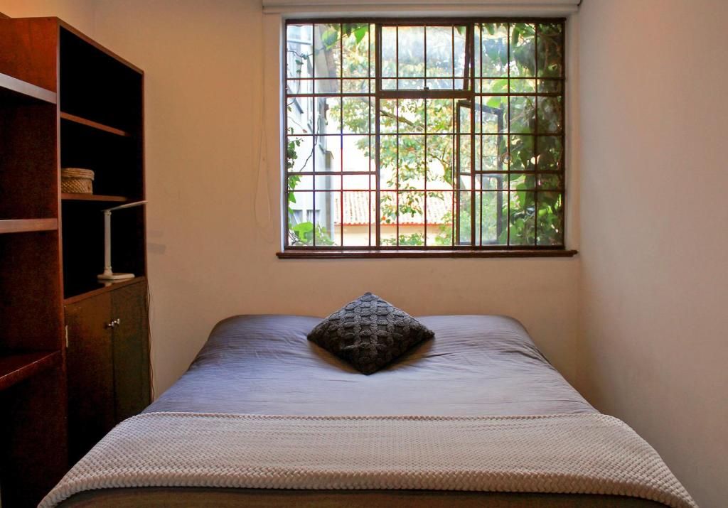 Un dormitorio con ventana, una cama con almohada y un armario de madera.