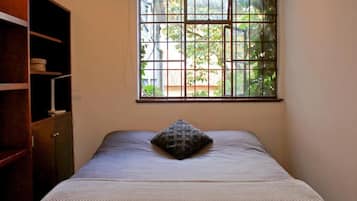 Un dormitorio con ventana, una cama con almohada y un armario de madera.