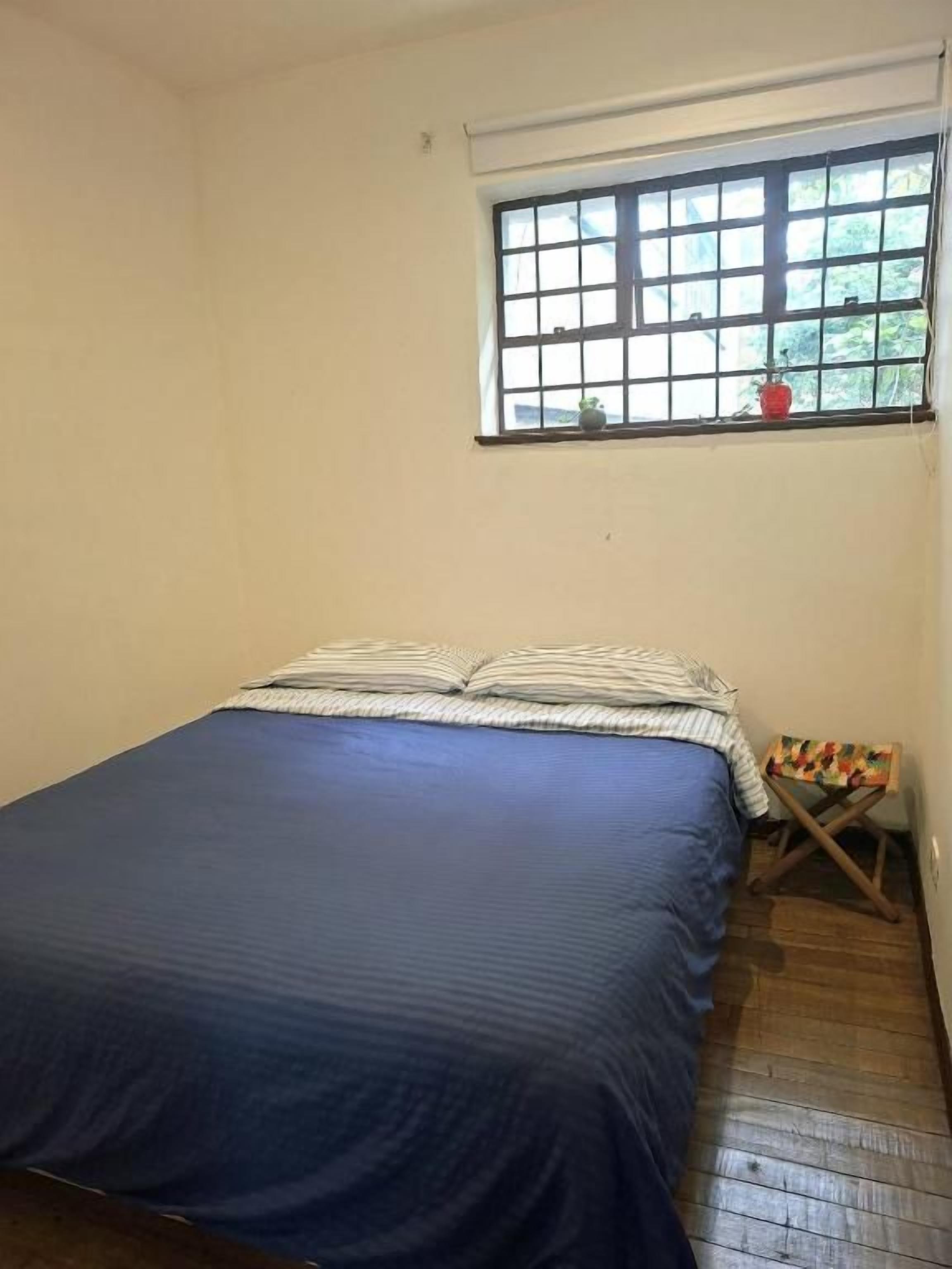 Una habitación con cama, ventana y una mesita con un mantel colorido.