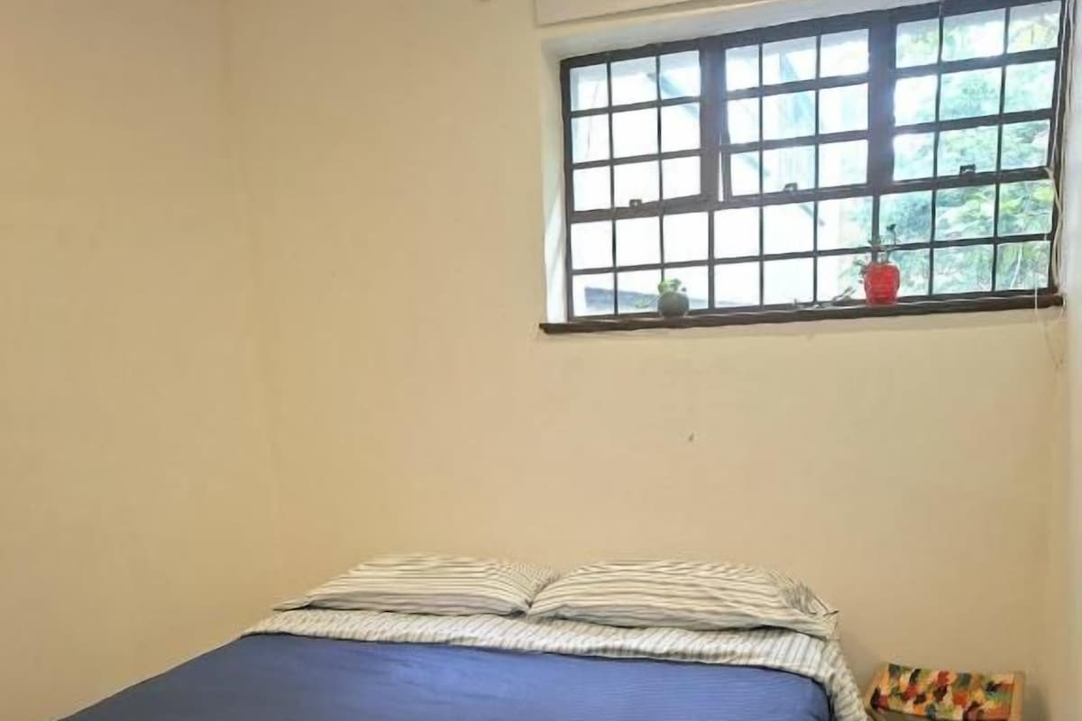 A room with a bed, a window, and a small table with a colorful cloth.