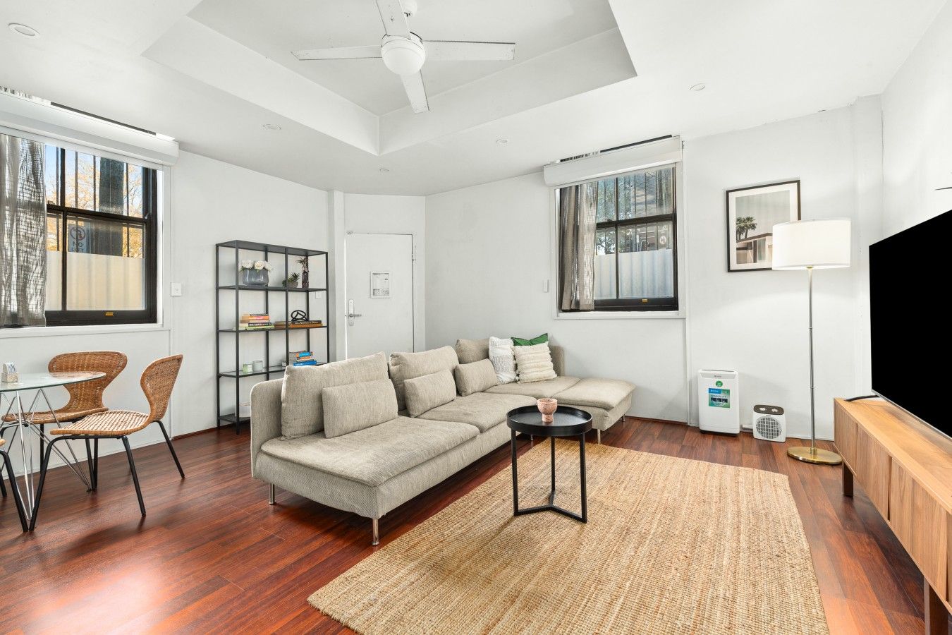 Een moderne woonkamer met een hoekbank, een eettafel met stoelen, een ventilatorkachel en een flatscreen televisie.
