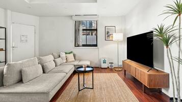 A modern living room with a sofa, a coffee table, a TV, a floor lamp, and a potted plant.