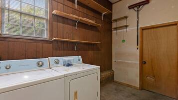A laundry room with a washer and dryer, wooden shelving, a broom, and a door.