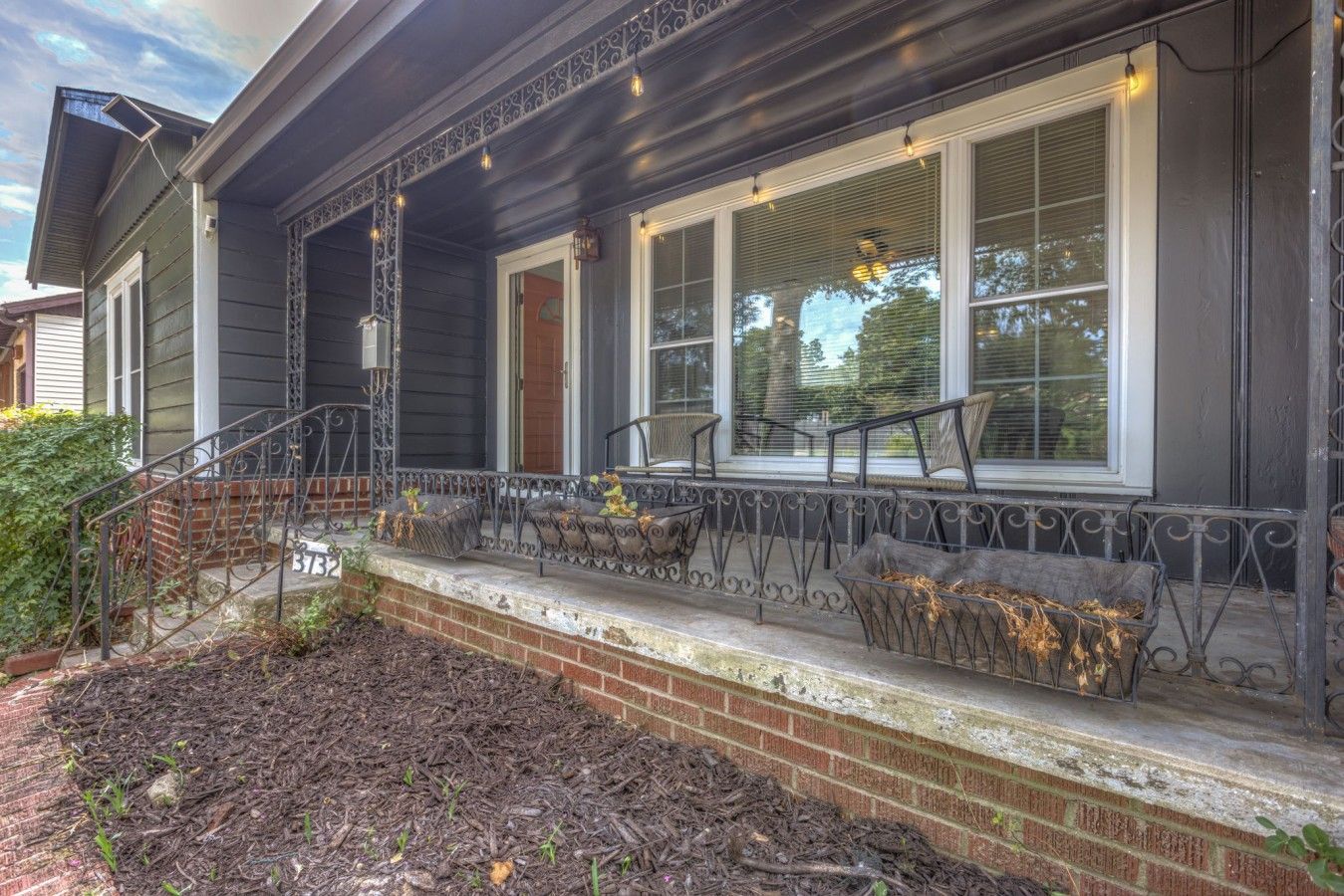 A house with a porch, a brick foundation, and a metal railing.