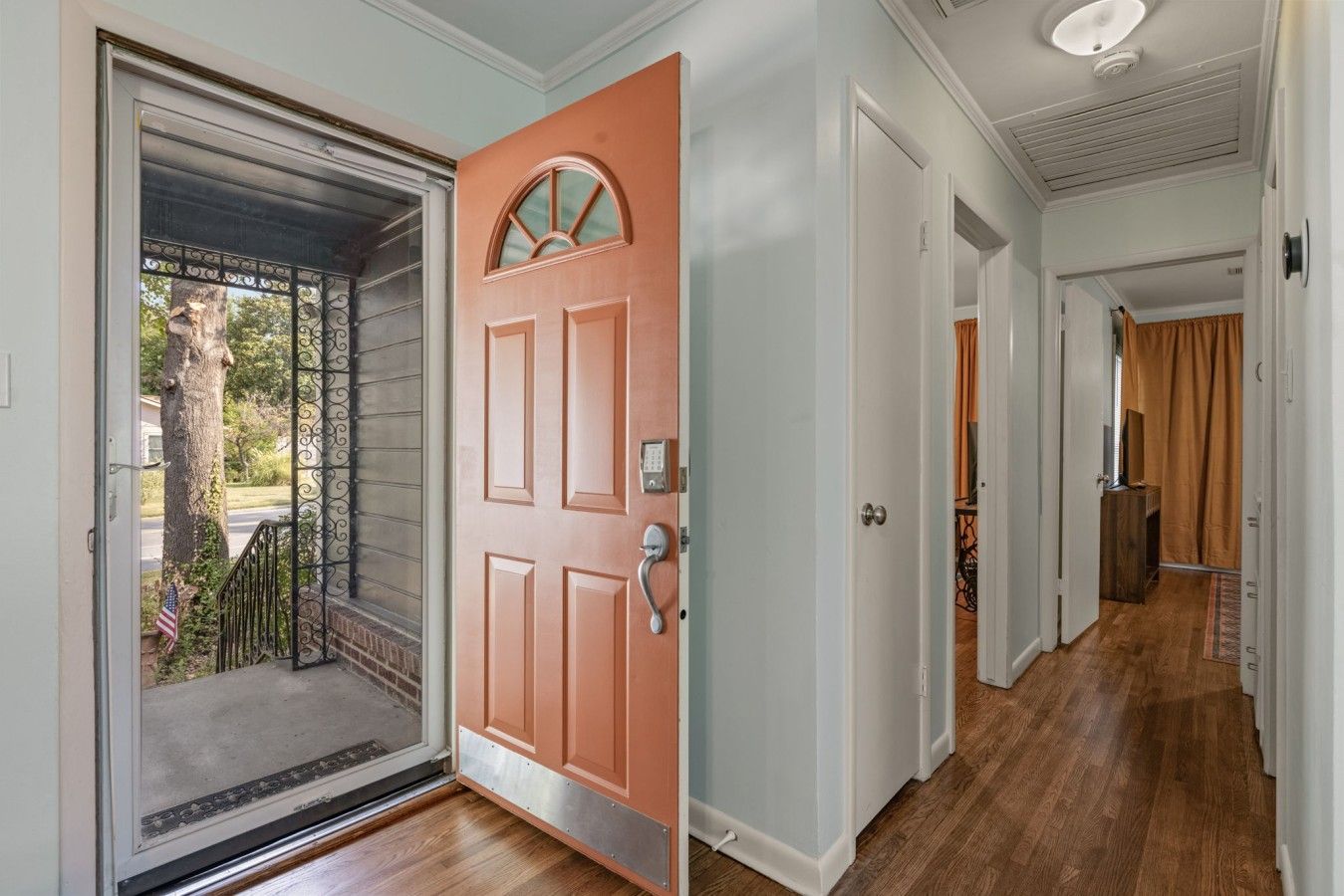 A hallway with a wooden floor, a door with a keypad lock, and a view of the outside.