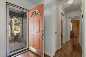 A hallway with a wooden floor, a door with a keypad lock, and a view of the outside. - Retro 2BR · King Bed · Pet-Friendly · TU & Expo (Tulsa)