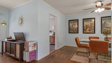 Un coin repas avec une table et des chaises en bois, un ventilateur de plafond et des tableaux représentant des paysages urbains accrochés au mur.