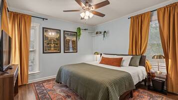 A bedroom with a bed, a ceiling fan, a TV, and a window with curtains.