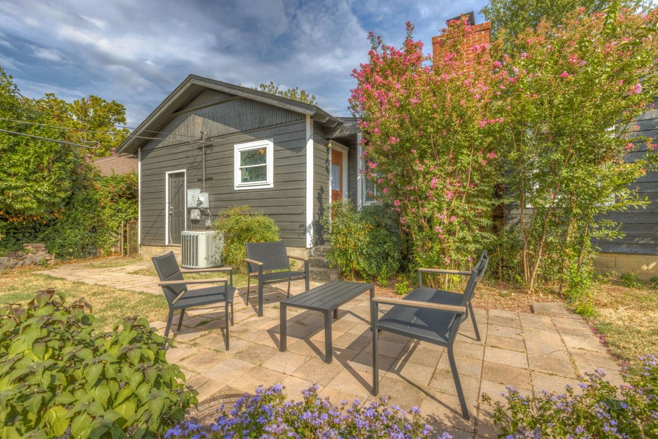 A house with a patio area featuring outdoor furniture and a garden with flowering plants.