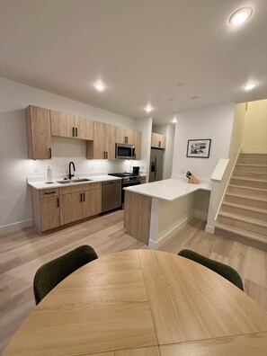 A modern kitchen with wooden cabinets, a central island, and a dining area with a round table. - Mountain getaway near Keystone, Breckenridge & Copper! Walk to shops & dining. (Silverthorne)